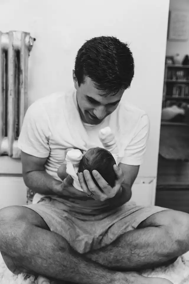Vater sitzt auf dem Boden und hält sein Neugeborenes im Arm